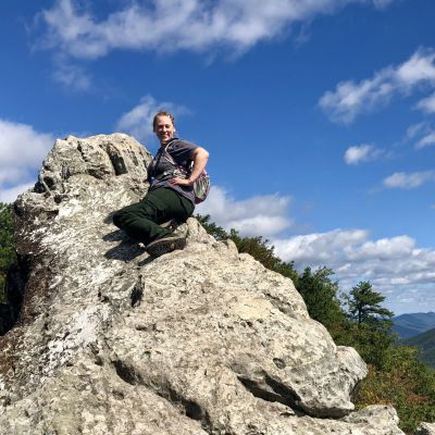 Ranger Beth Christensen sitting on the rock of Drangon's Tooth, a popular hike on the Appalachian Trail in the George Washington & Jefferson National Forests