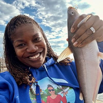 Rivah Sistah Patricia Clement fishing on Rappahanock River in Urbanna, Middlesex County, Virginia. Holding a large fish, wearing a blue hoodie showing image of river life.