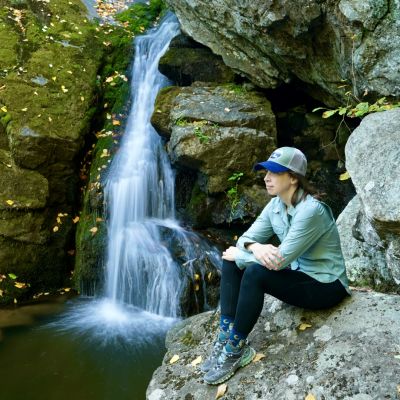 Female hiker sitting on a rock at the base of a small waterfall in the Blue Ridge Mountains in autumn