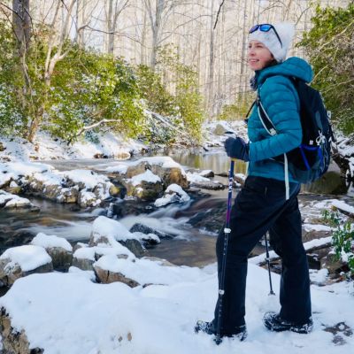 Jessica Bowser, Host of Virginia Outdoor Adventures Podcast, hiking in the snow next to a forest stream.