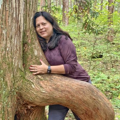 Ana Ka'ahanui, podcast guest featuring forest bathing, leaning against the trunk of a cypress tree, hugging the tree.