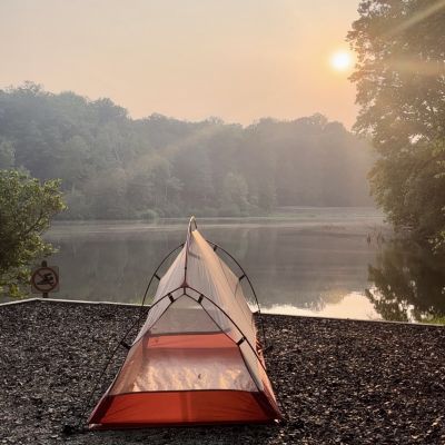 Tent on a campground next to a lake and a setting sun.
