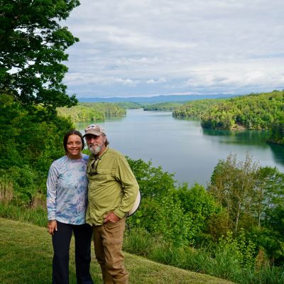 Anna Wheeler and Brian Williams stand at the observation point at Philpott Lake. Mountain lake surrounded by tress and blue sky.