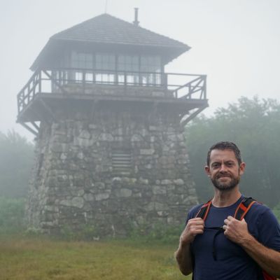 Vince Mier, episode guest and district manager of Walkabout Outfitter, stands in front of High Knob Fire Tower in the Washington National Forest on a foggy evening.